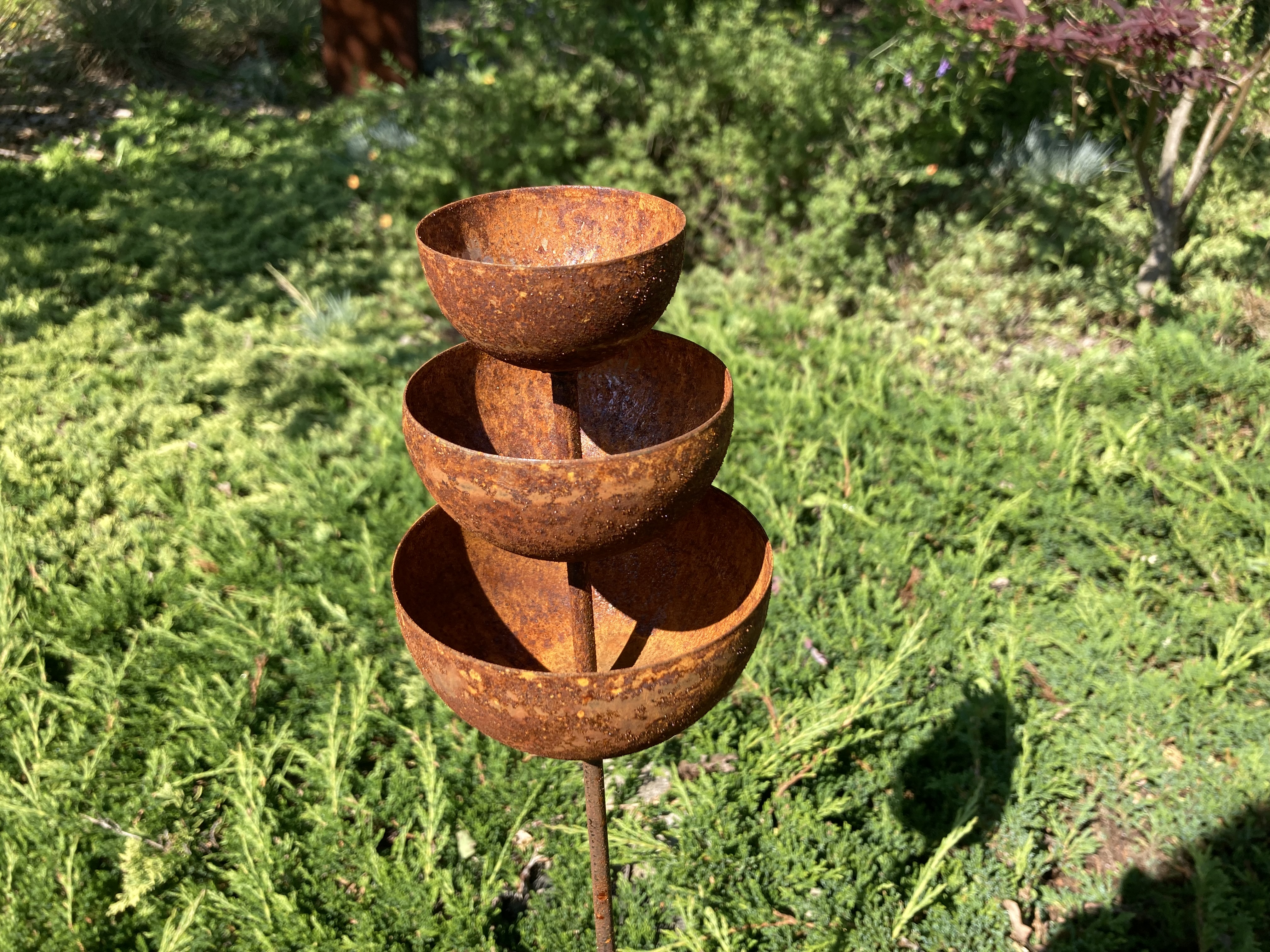 Rustykalne poidełko ogrodowe z metalu pokrytego rdzawą patyną od Ginko Garden na tle zieleni – dekoracja w stylu Martha Stewart aesthetic